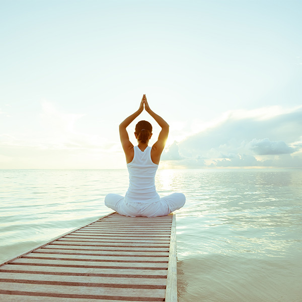 a woman sitting in a meditative pose at the end of a dock overlooking water