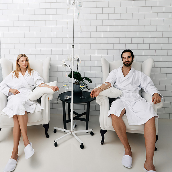 Man and a woman dressed in white robes receiving nutrients through IV hydration therapy