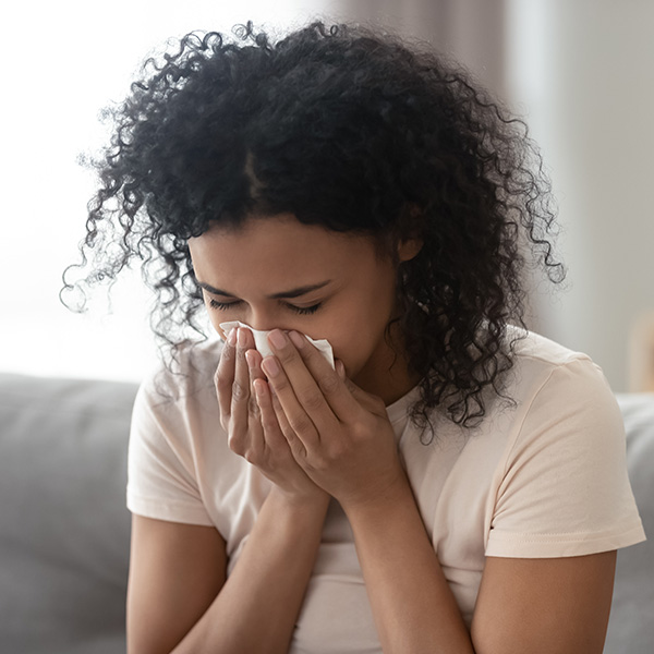 woman sitting on the couch sneezing into a white tissue