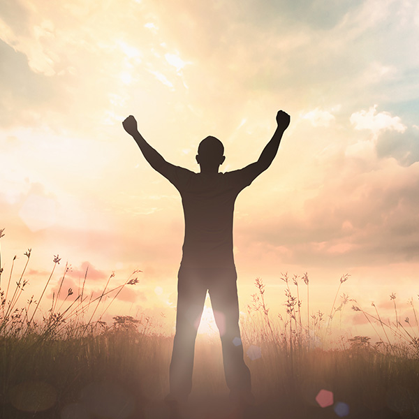 Man standing in a field with his arms raised while the sun is setting